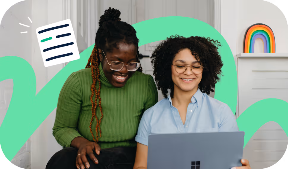 Two women with glasses smiling while looking at a laptop screen together indoors.