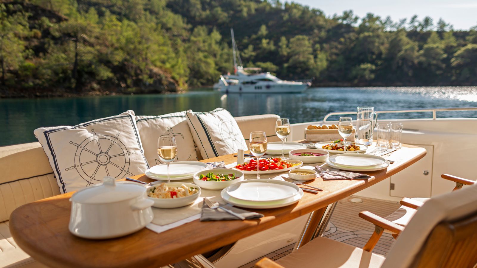 A yacht dining table set with wine glasses and fresh dishes overlooking a calm bay — perfect for a first charter experience.