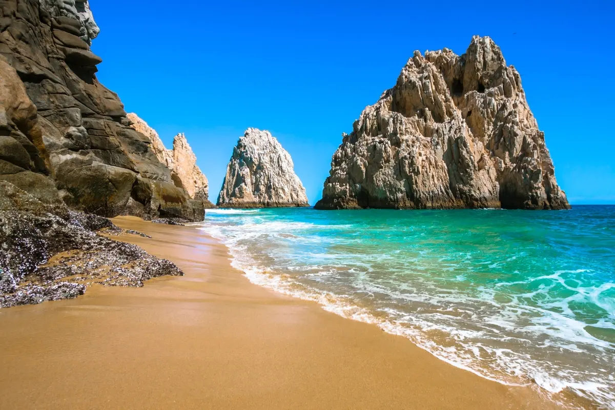 Golden sandy beach in Cabo San Lucas, Baja California, with turquoise waves and dramatic rock formations.