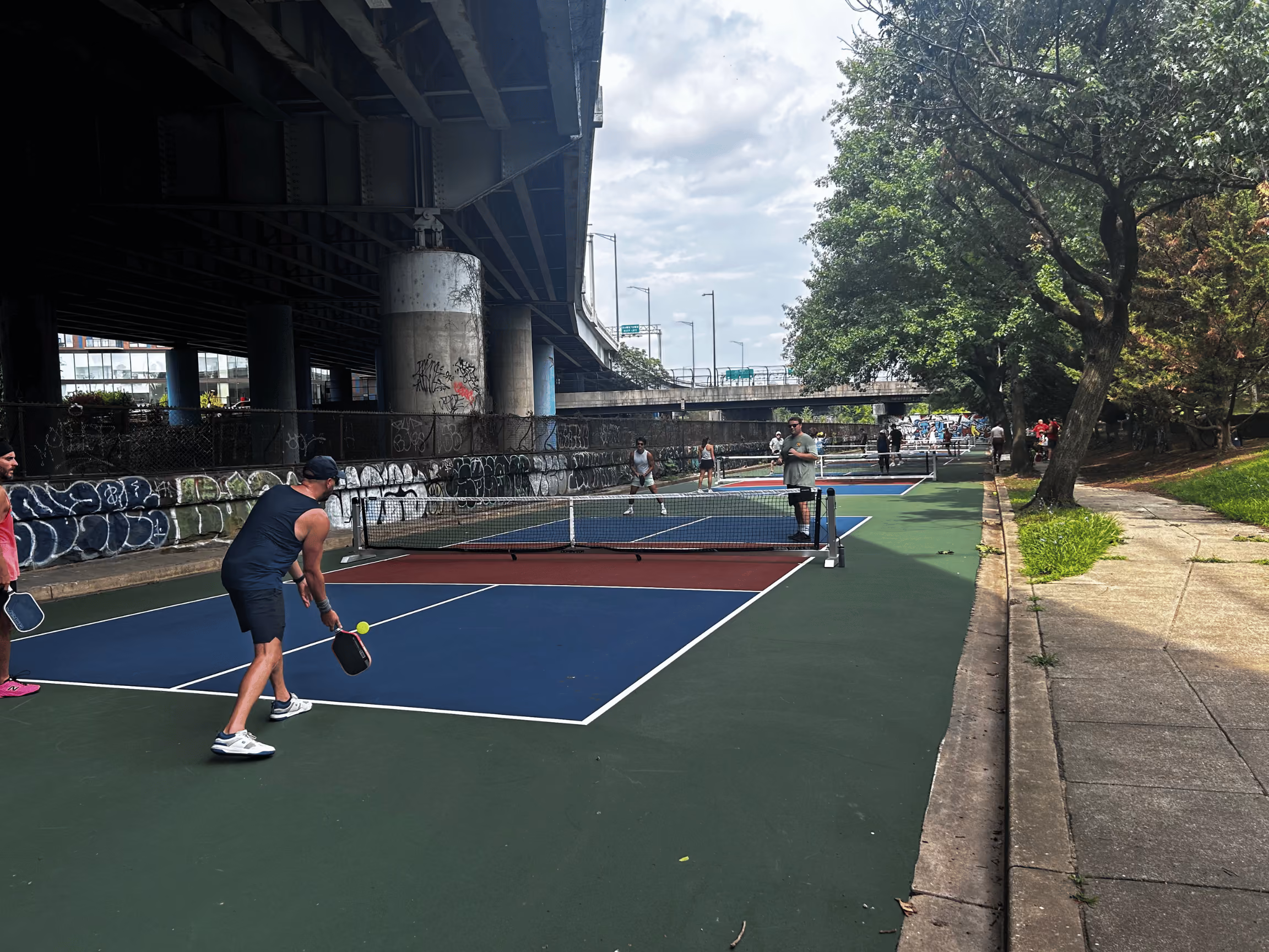 Open play on the Krughoff courts on a sunny day, with the freeway on one side and trees on the other