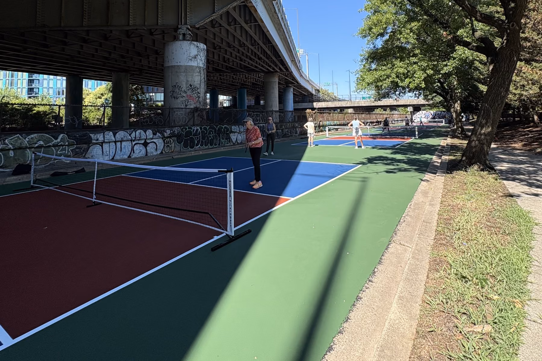 Players on the Krughoff Pickleball Center courts beneath the freeway on a sunny afternoon