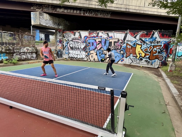 Two players on a court in front of a graffiti wall beneath the freeway at Bridge Spot