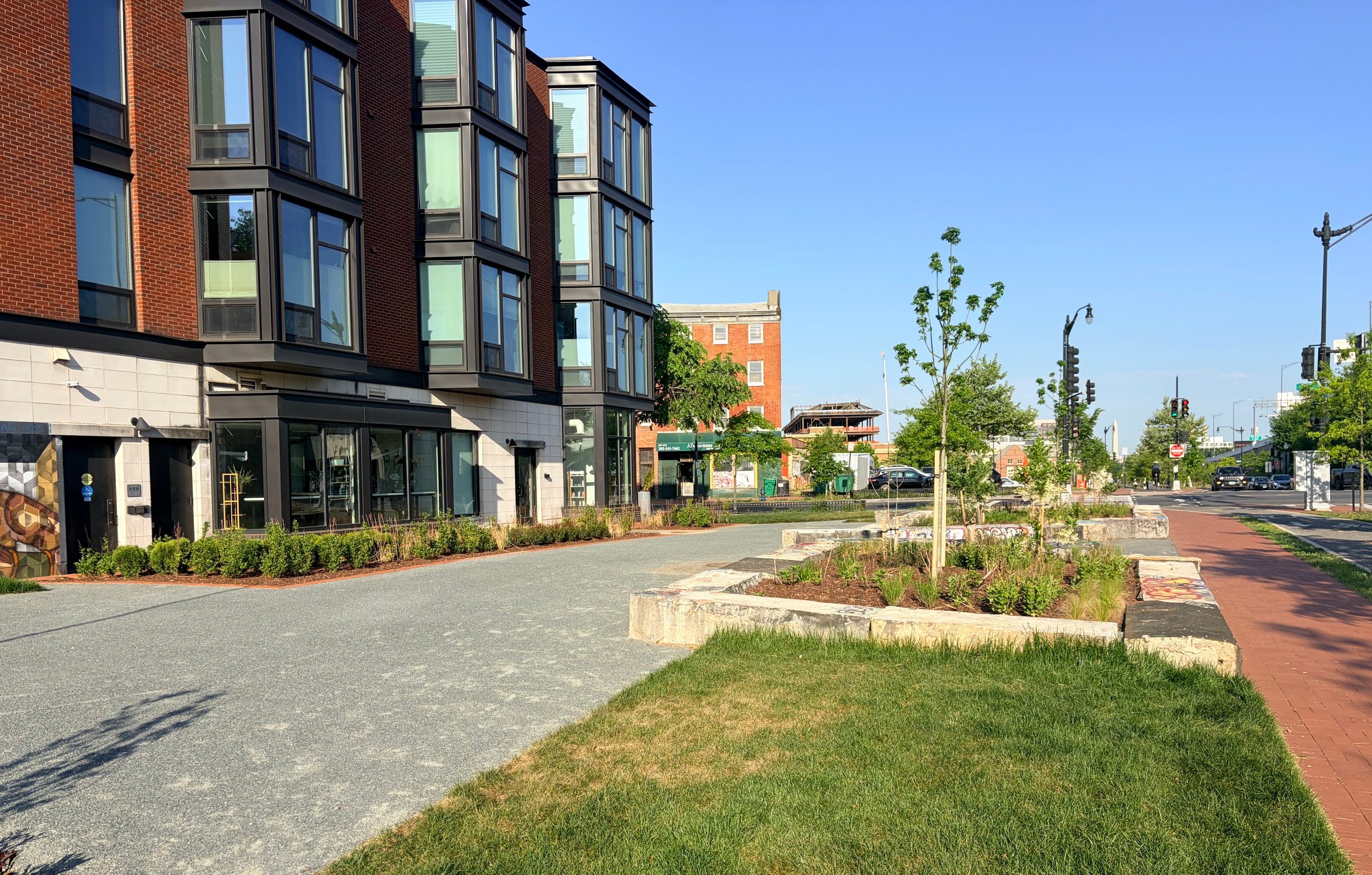 Emblem Plaza in evening sun, with a new lawn, planting beds and young trees, and the Washington Monument in the distance