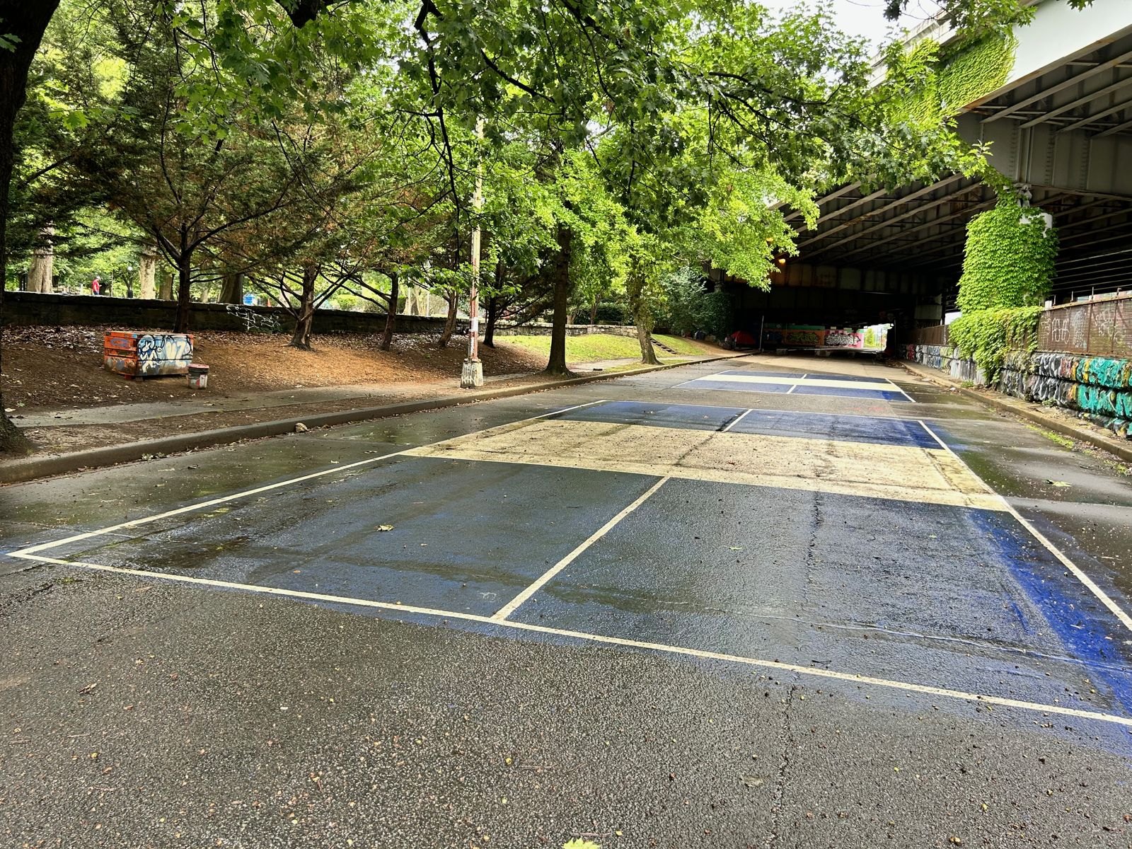 The empty, cracked roadway under the freeway, with faded lines, before it became courts