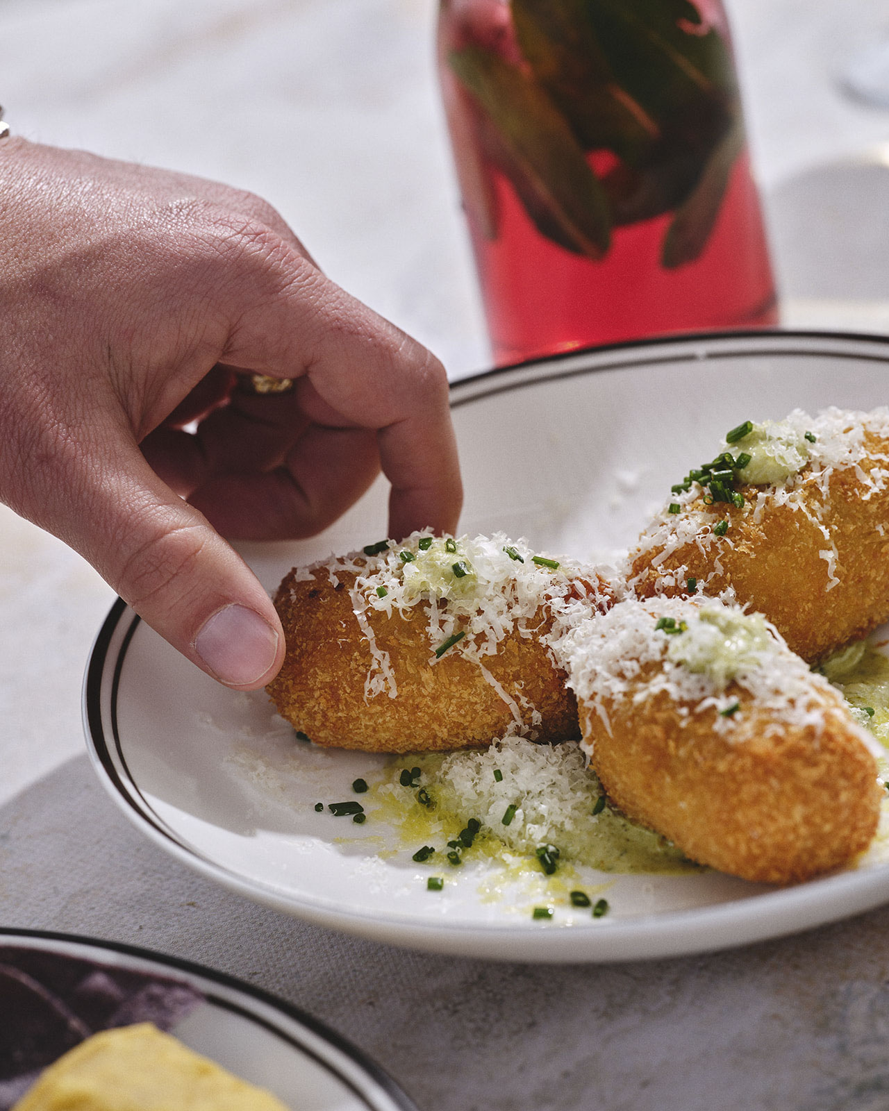 A wooden board with sausage rolls, sliced cheese, and cured meat on a table. In the background, a tray of raspberries and other snacks. Cozy brunch setting.