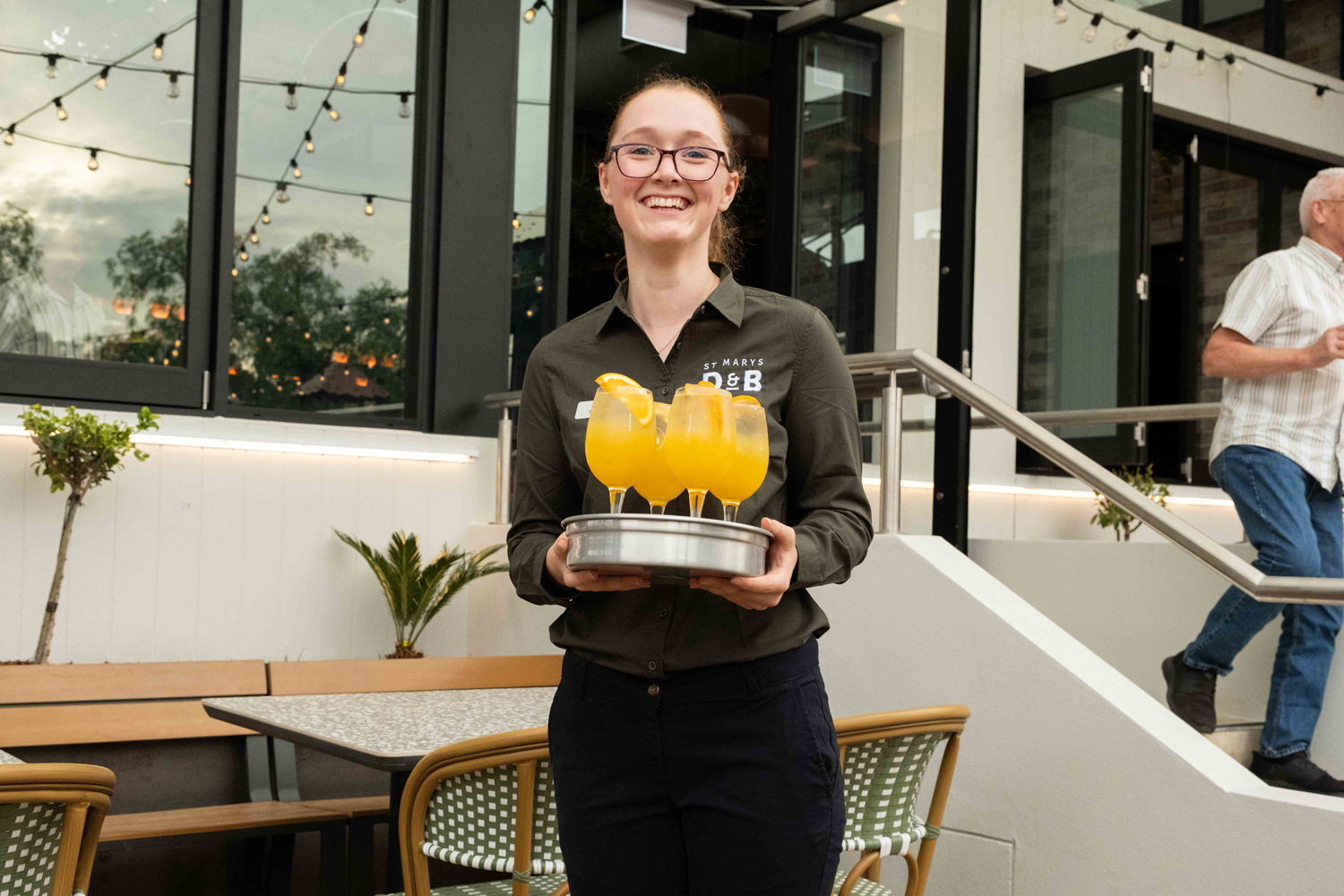 Chef in a white uniform and gray apron focuses intently while pouring sauce from a pot onto a dish, creating a calm, professional atmosphere.