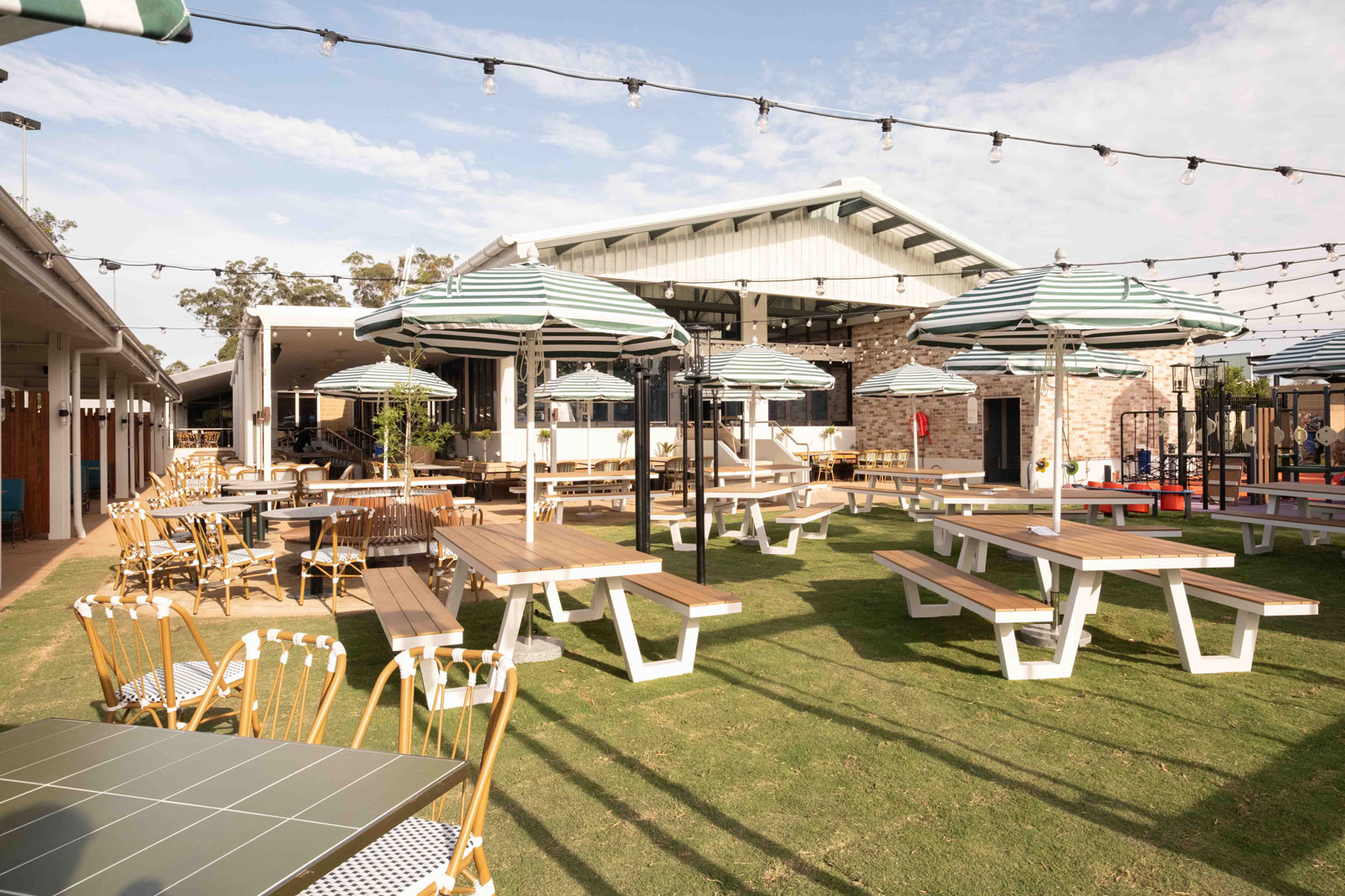 A group of six people sit around a wooden table, engaged in animated conversation, with wine glasses and plates of food. Hanging plants create a relaxing ambiance.