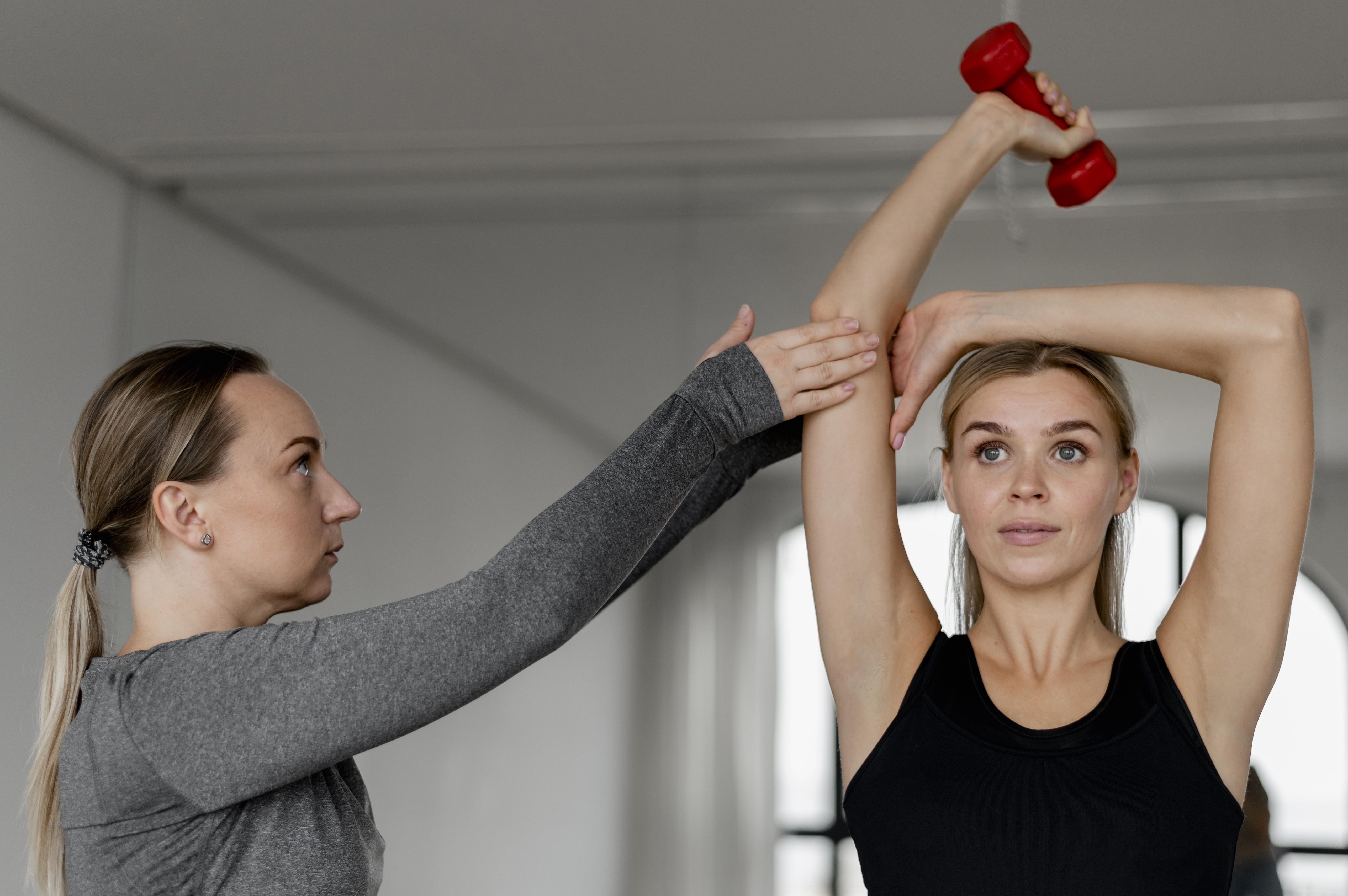 Two women doing exercises with red dumbbells.