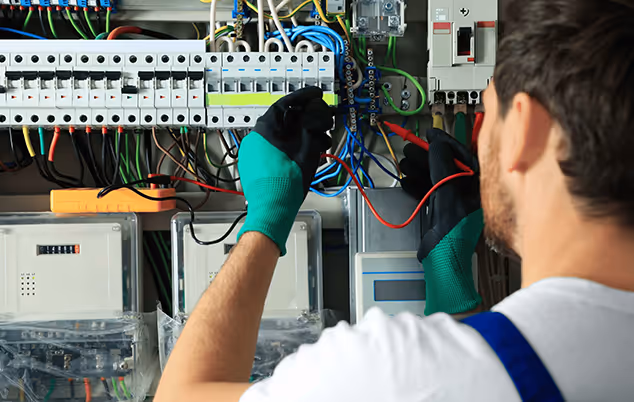 Electrician wearing green gloves connecting wires inside an electrical panel