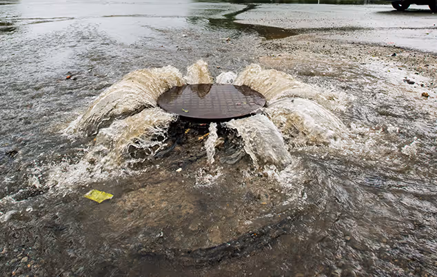 A manhole surrounded by water in a flooded street, highlighting urban flooding conditions.