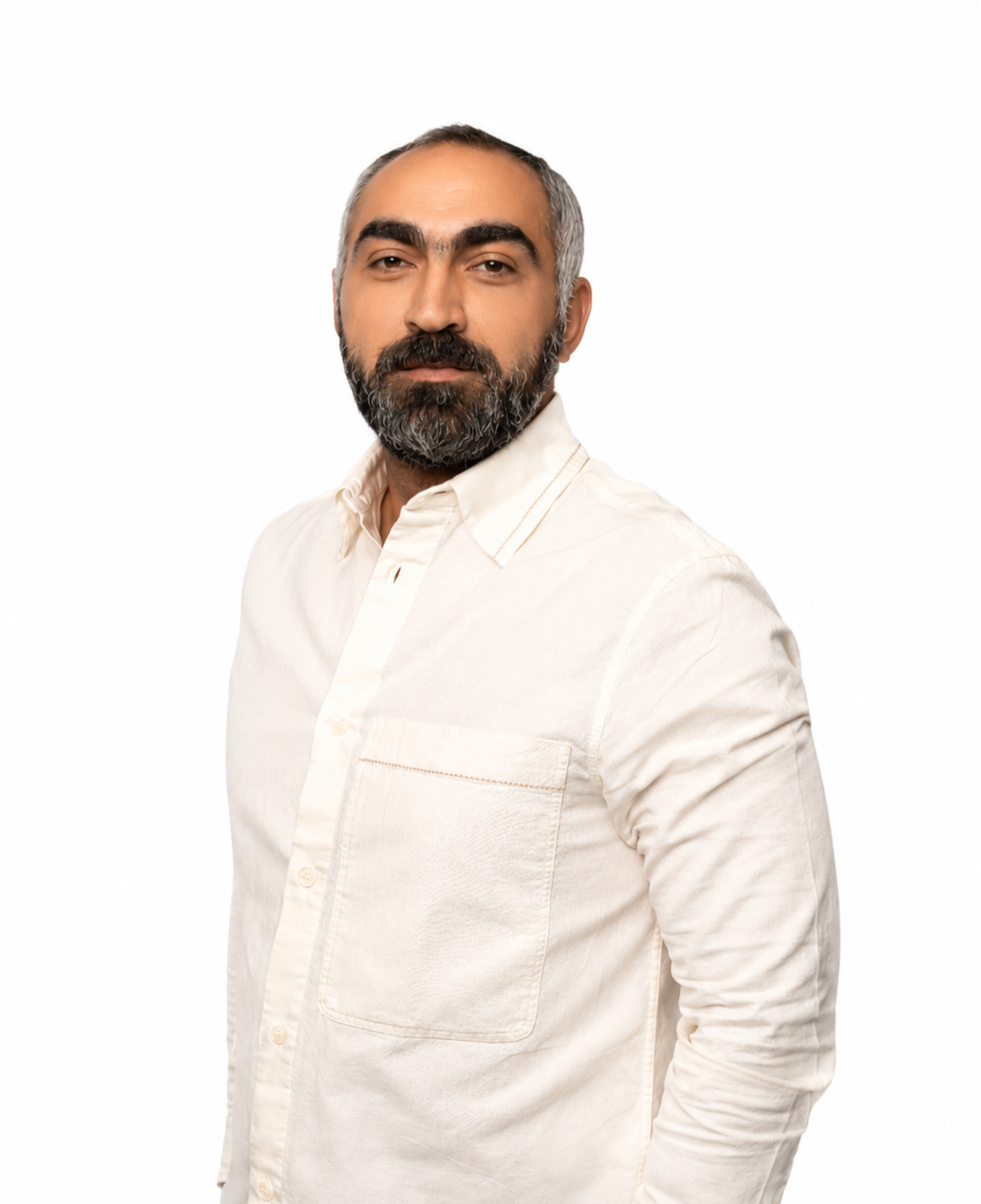 Professional portrait of a man with short salt-and-pepper hair and a full beard, wearing a white button-up shirt and standing against a clean white background.