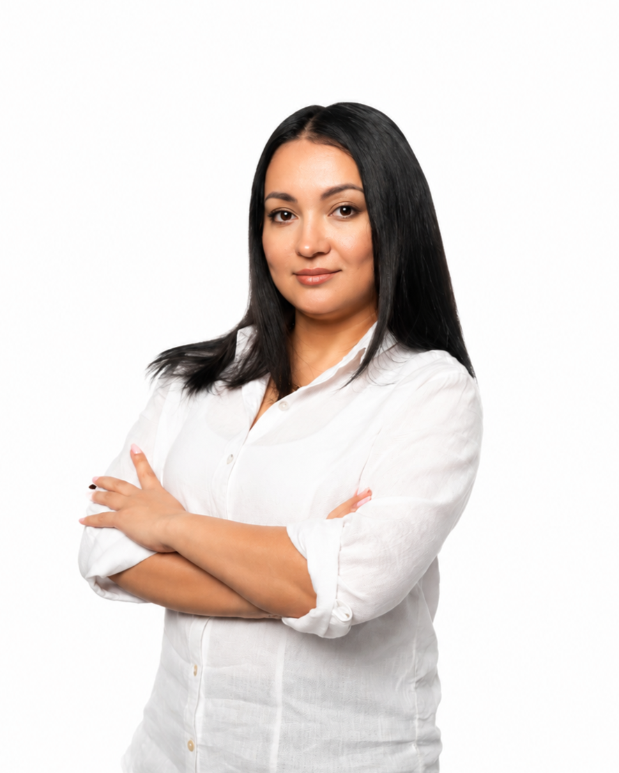 Professional portrait of a woman wearing a sleeveless white blouse and black pants, standing confidently against a clean white background.