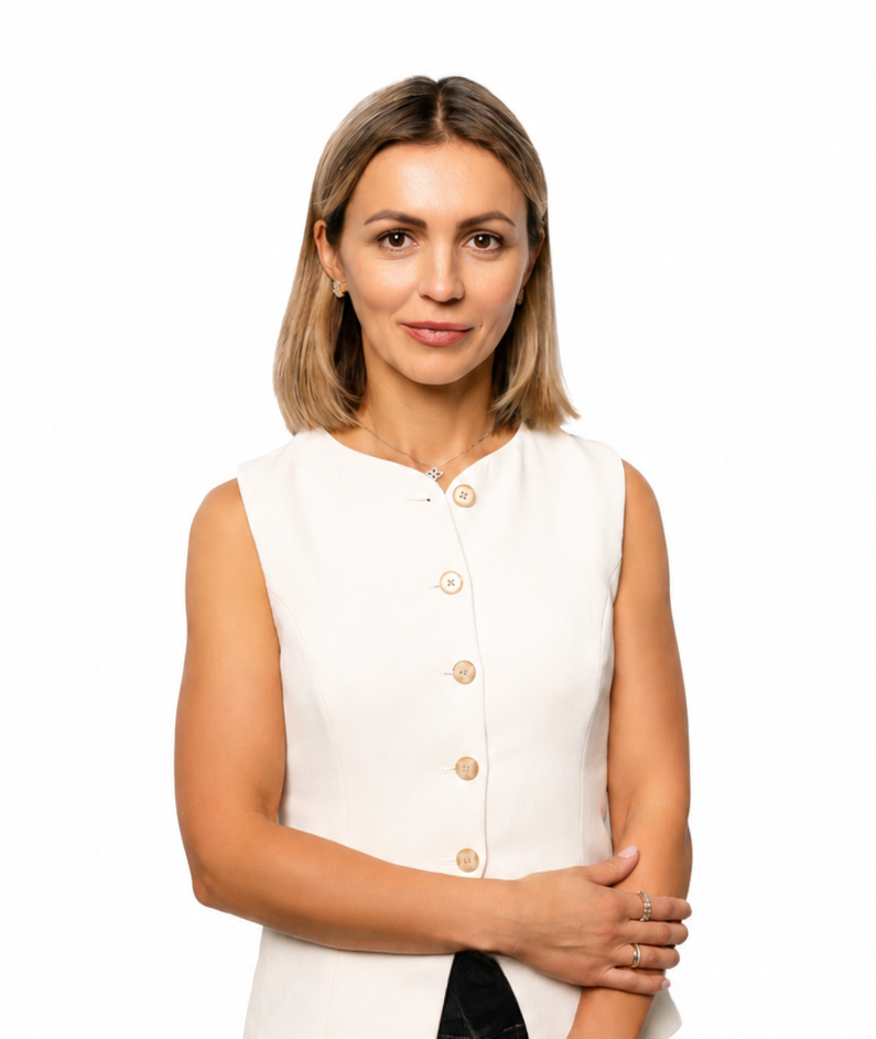 Professional portrait of a woman wearing a sleeveless white blouse and black pants, standing confidently against a clean white background.
