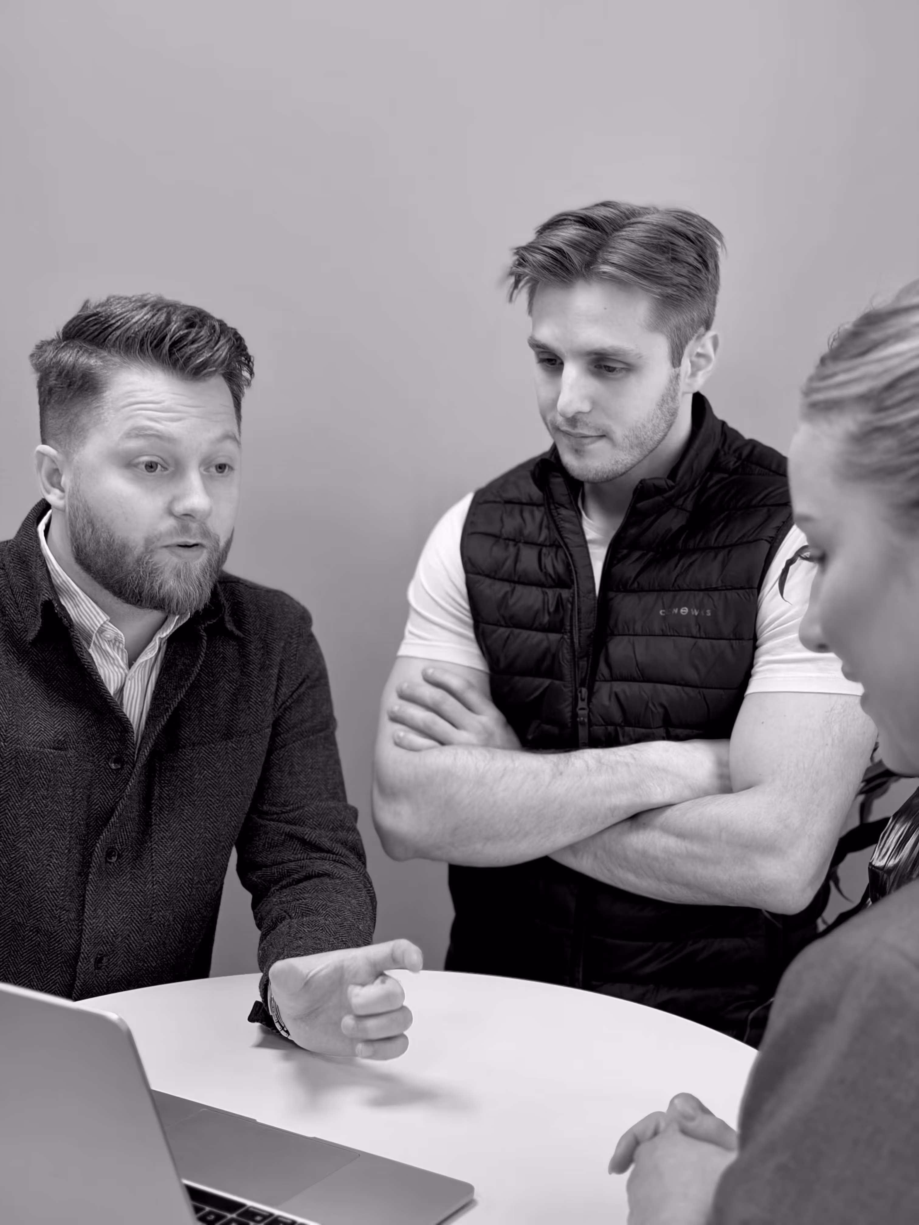 Tre personer, två män och en kvinna, sitter vid ett bord och diskuterar medan de tittar på en bärbar dator.
