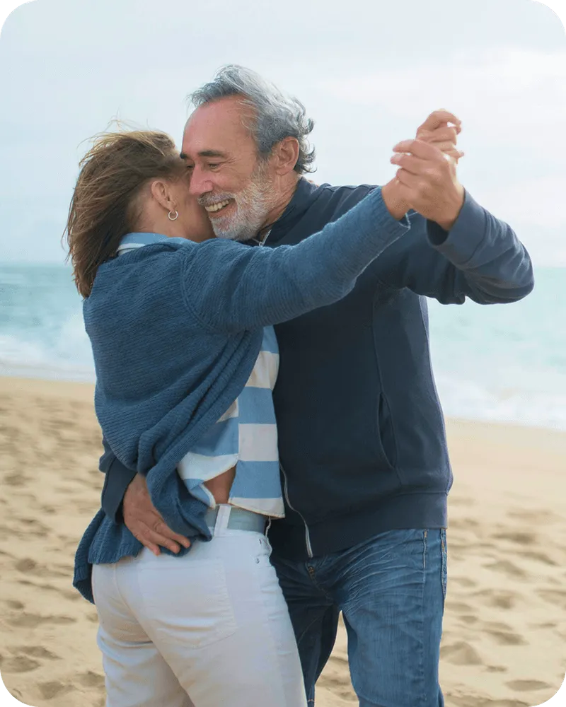 Happy senior couple dancing playfully on the beach, enjoying a moment together by the sea