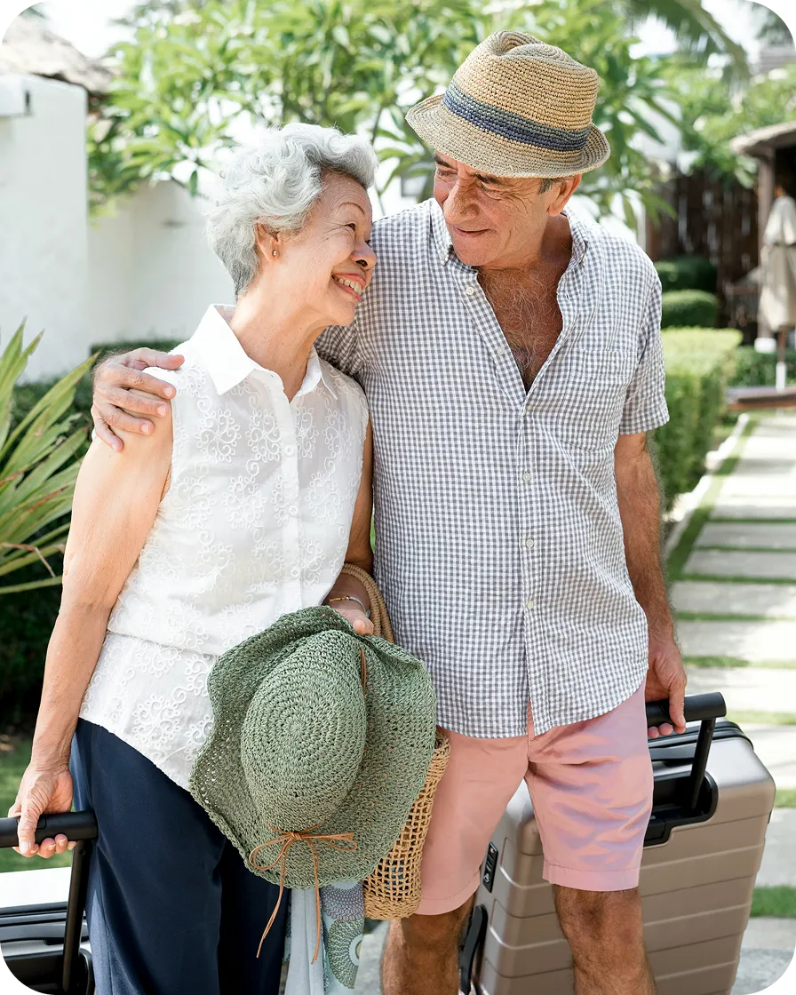 An elderly couple walking together outdoors with suitcases, smiling at each other while enjoying a vacation.