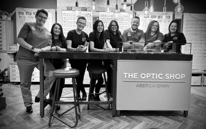 Optic shop team posing together behind counter in black and white