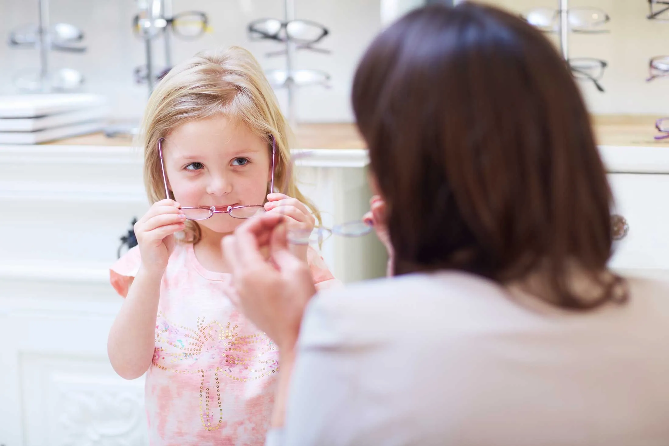 Young girl trying on glasses at optometrist with adult assistant