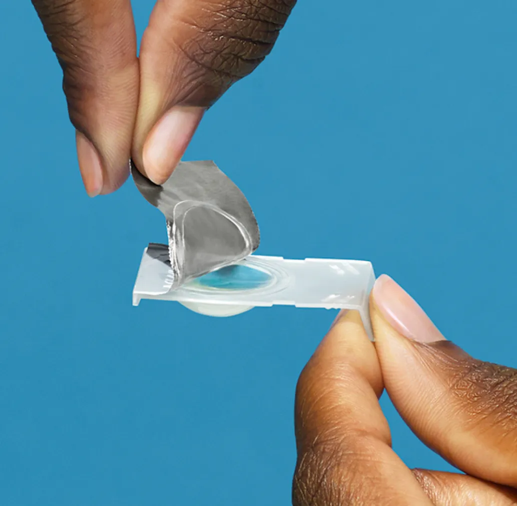 Hands opening a medical test strip with a blue liquid sample