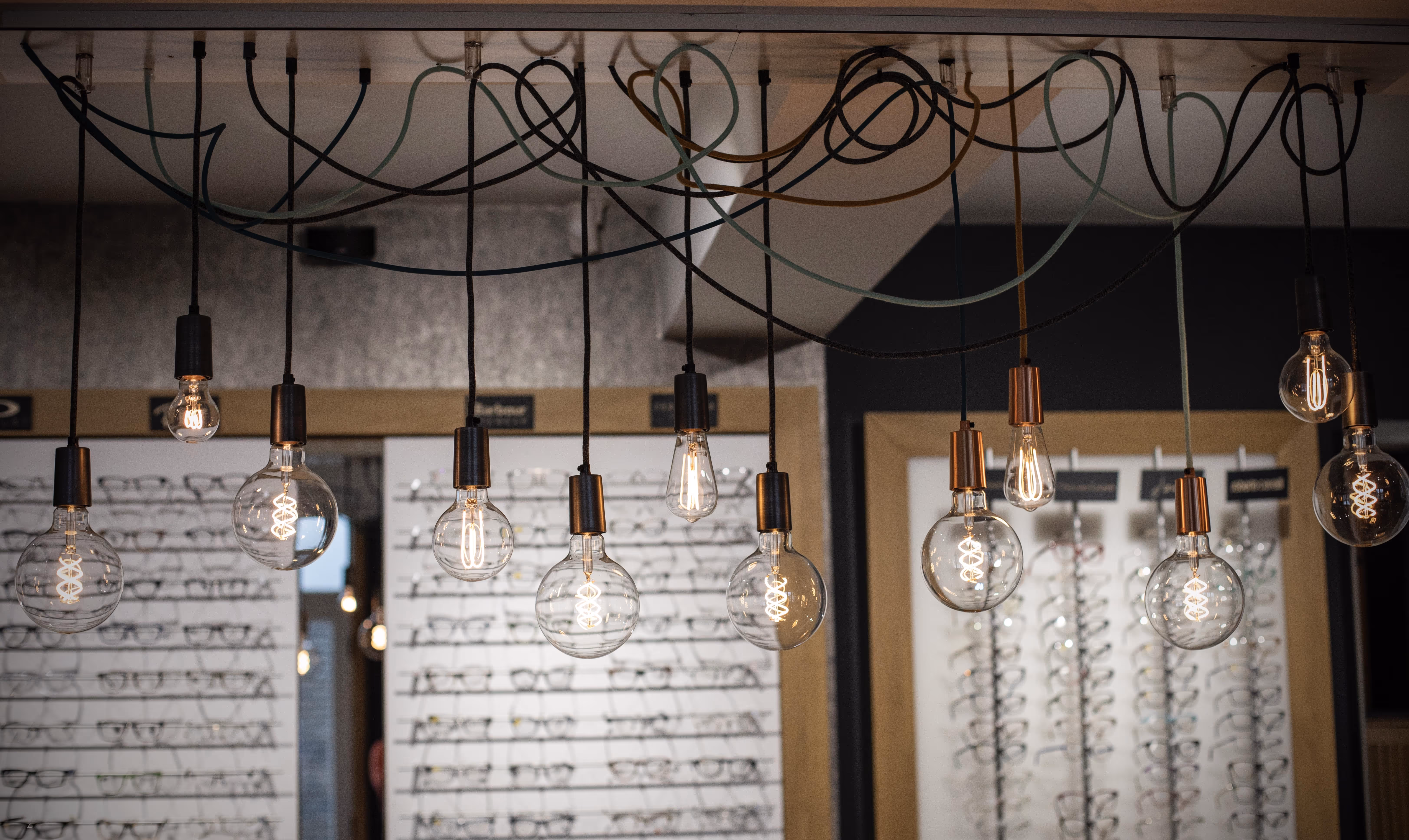 Vintage Edison bulbs hanging from tangled wires in modern eyeglass shop