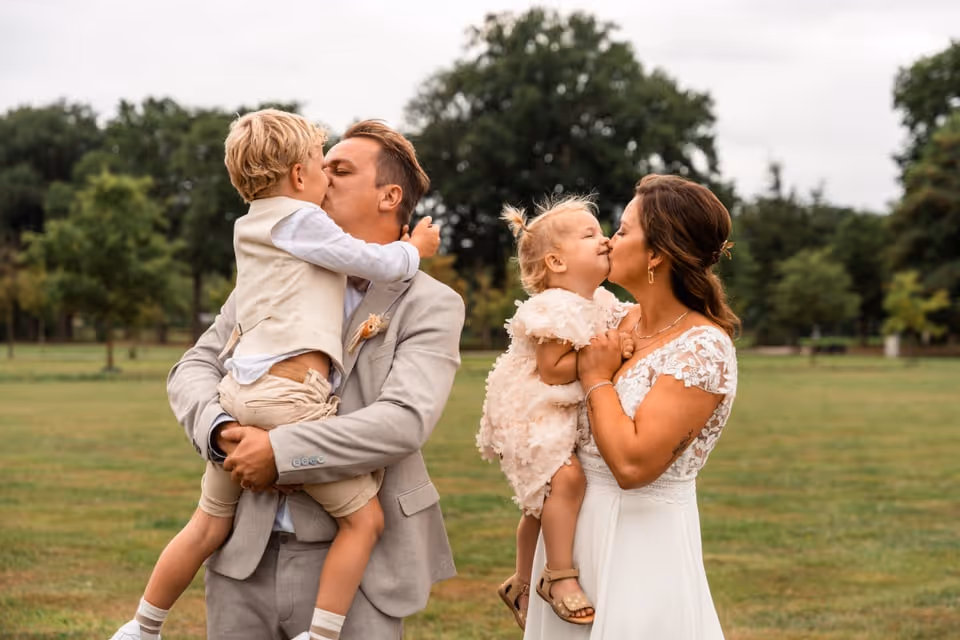 Lieve familiefoto waarbij de bruid haar dochter een kus geeft en de bruidegom zijn zoon een kus geeft.