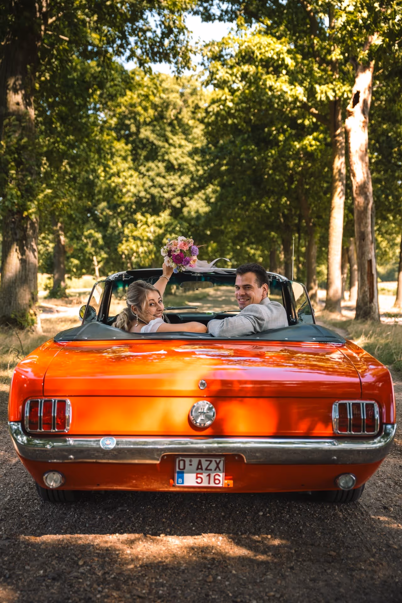 Een bruidspaar poseert in een rode cabrio. De bruid houdt haar bruidsboeket in de lucht.