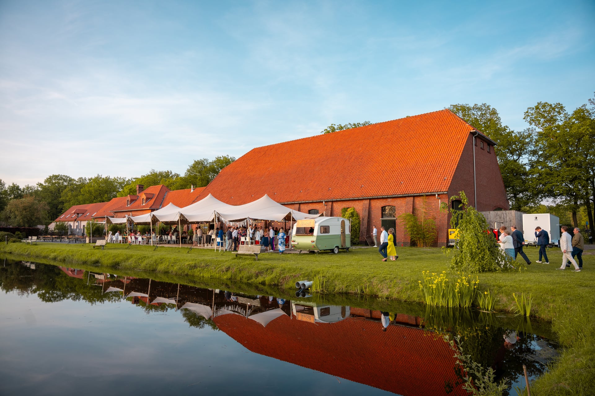Trouwlocatie buiten aan een vijver, met foodtruck, open tenten en gasten.