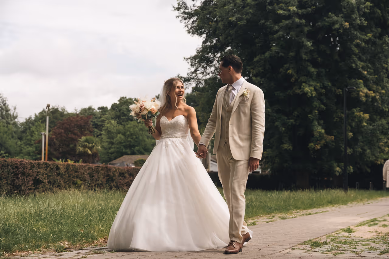 Het bruidspaar loopt hand in hand en lacht liefdevol naar elkaar.