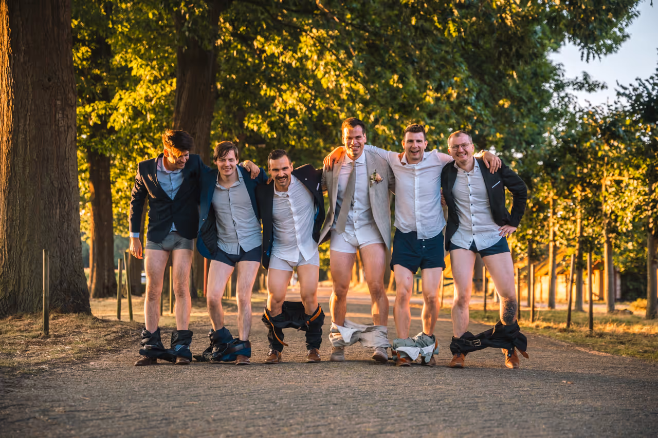 6 gasten poseren al lachend voor de camera met hun broek op de enkels.
