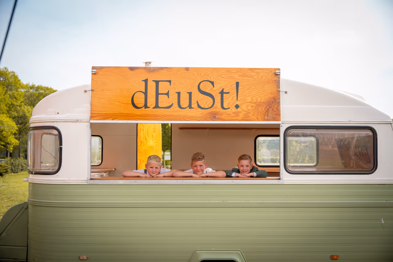 Foodtruck dEuSt! met 3 kinderen die op de toog leunen en lachen naar de camera.
