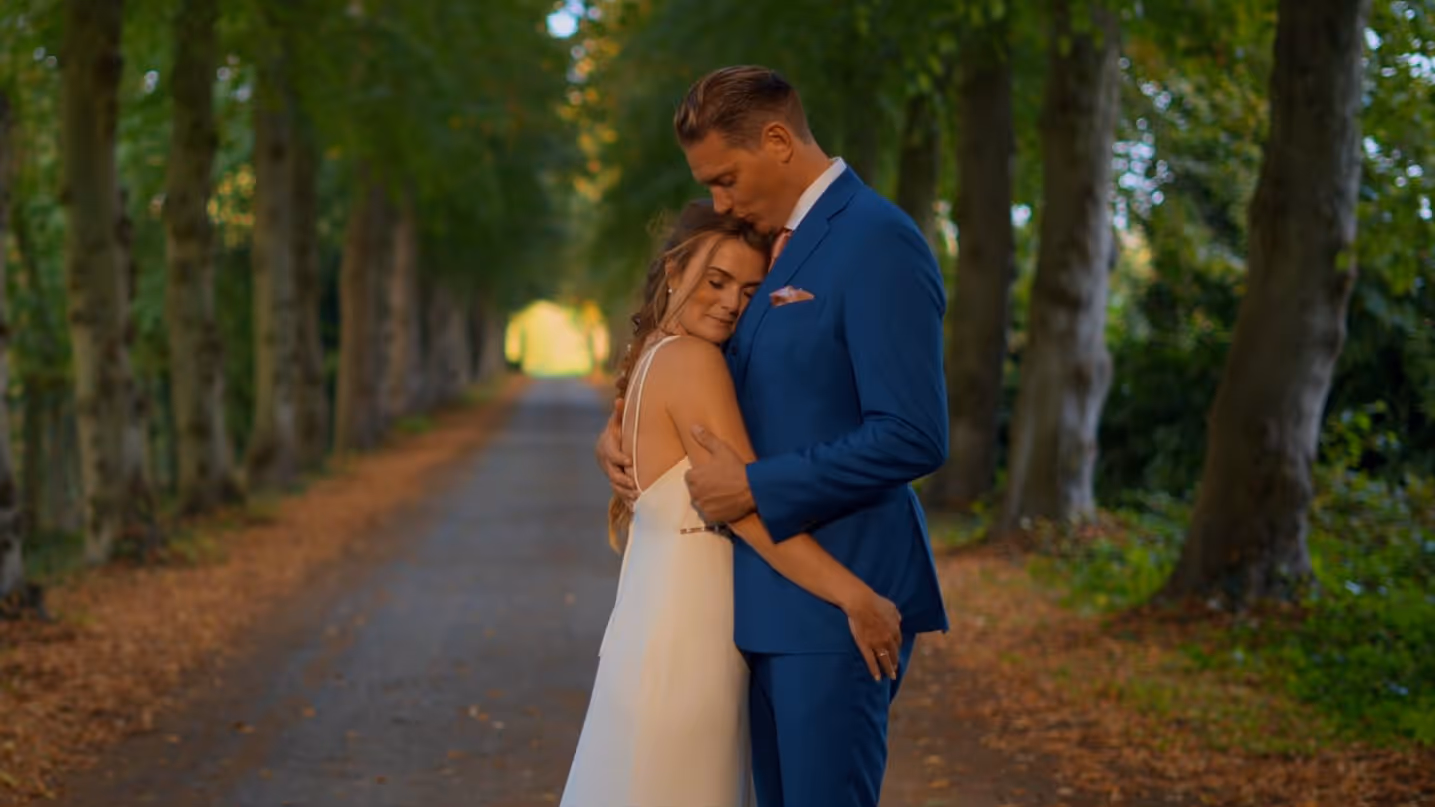 Bruidegom in een blauw kostuum geeft zijn witte bruid een kus op het hoofd.