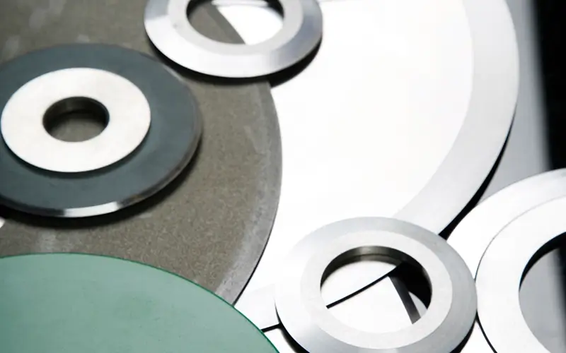 Assortment of circular knives with polished cutting edges and central holes, manufactured by Durham Duplex for easy cleaning and corrosion resistance.