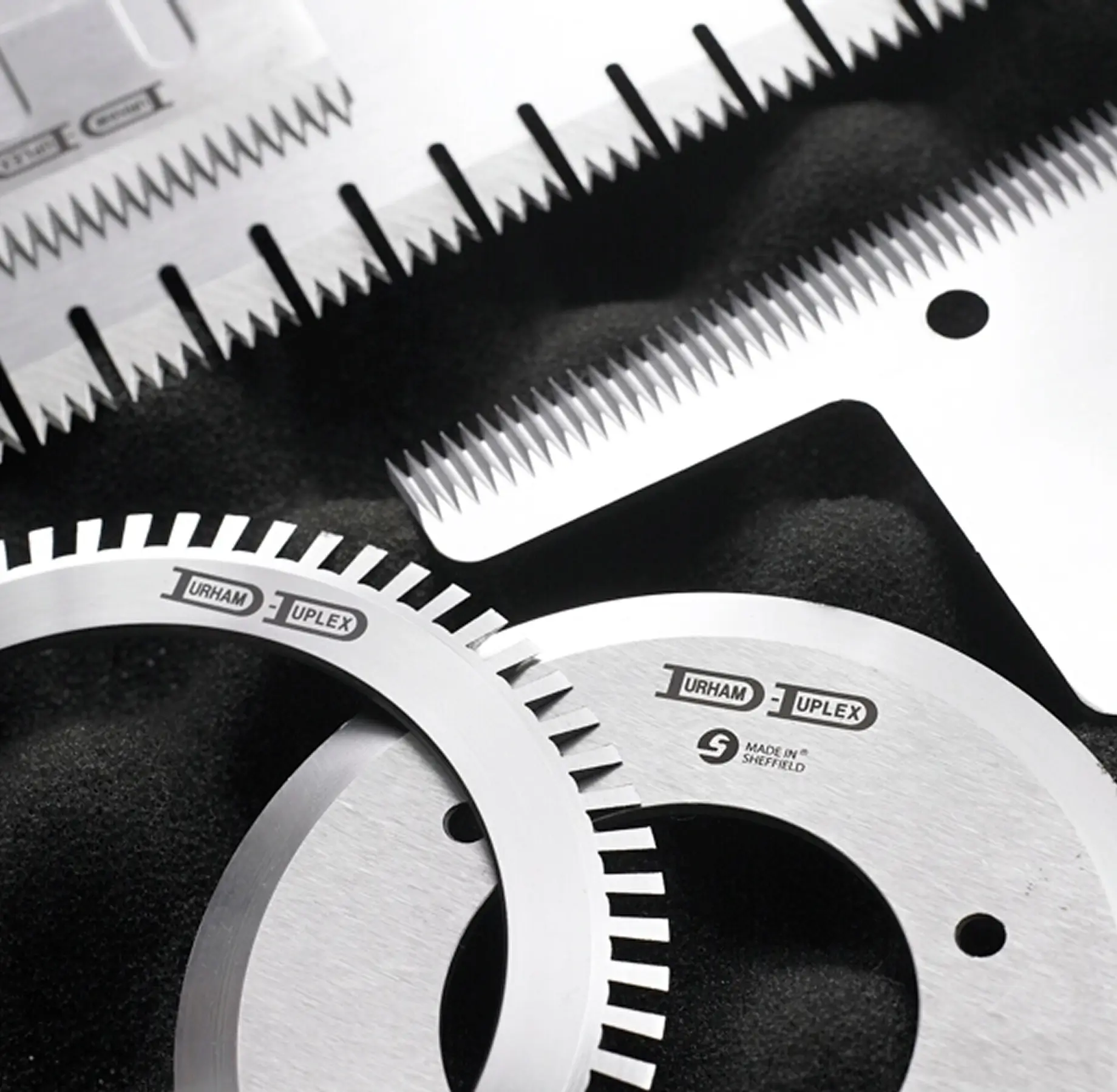 Close up image of metal industrial cutting blades, including a circular saw-style discs with fine teeth placed on a dark background, showcasing Durham Duplex expertise in high-quality knife manufacturing.