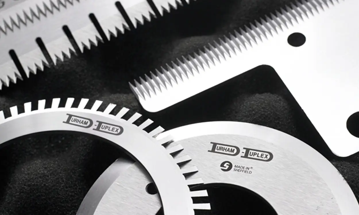 Assortment of serrated and circular industrial knives engraved with Durham Duplex logo, showcasing precision blades for packaging and cutting application.