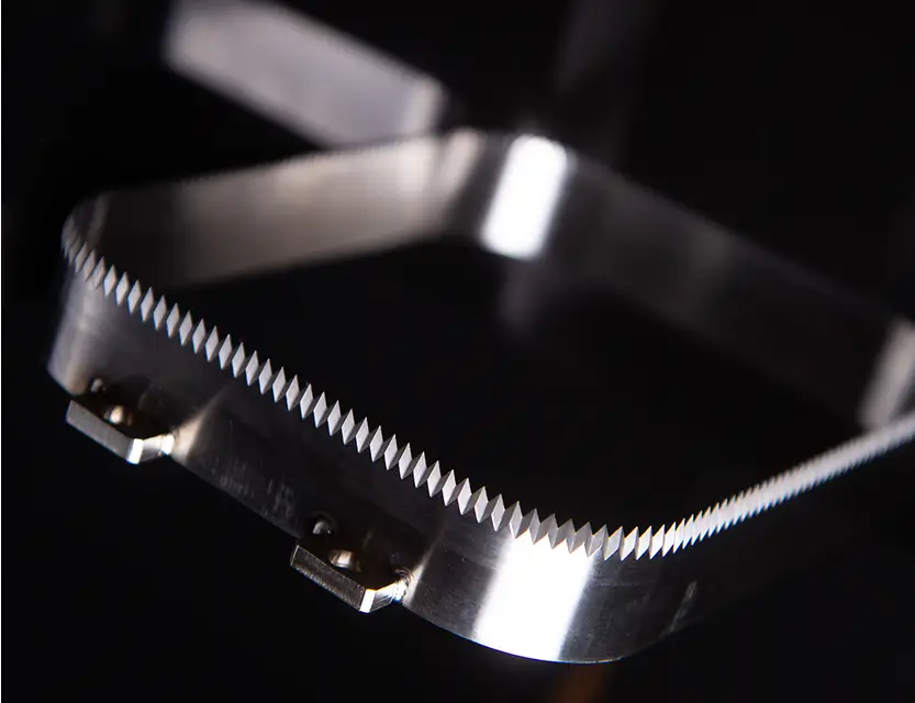 Close-up of a stainless steel tray knife with fine serrated edges, used in packaging applications and manufactured by Durham Duplex.