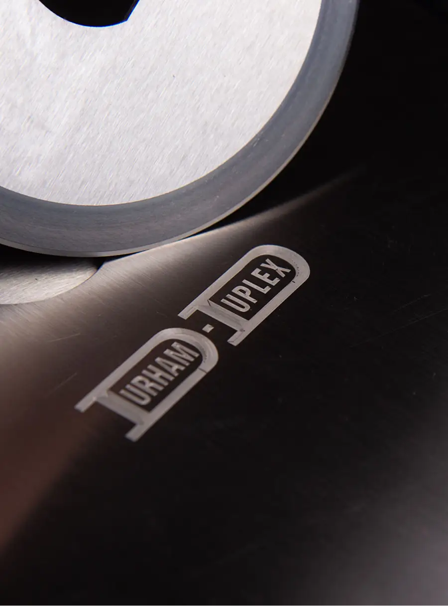 Close-up of a circular industrial blade engraved with the Durham Duplex logo, showcasing precision knife manufacturing. 