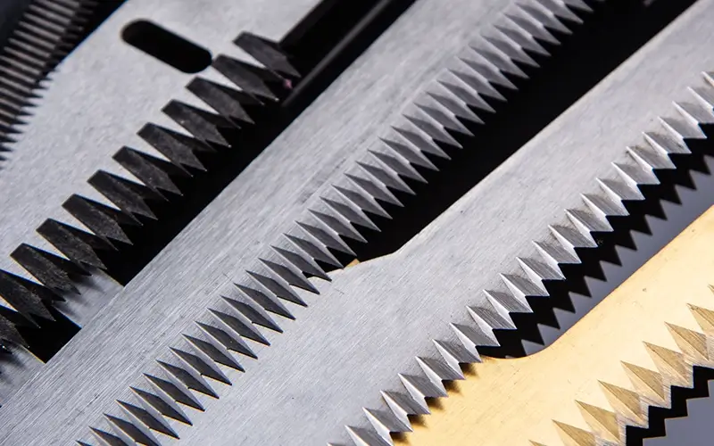 Close-up of serrated flow wrap knives in steel and gold finishes, manufactured by Durham Duplex.