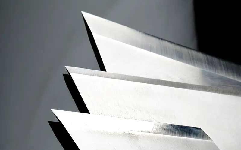 Sharp piercing knives with angled pointed edges, aligned in a row on a reflective surface, manufactured by Durham Duplex for precision cutting application.