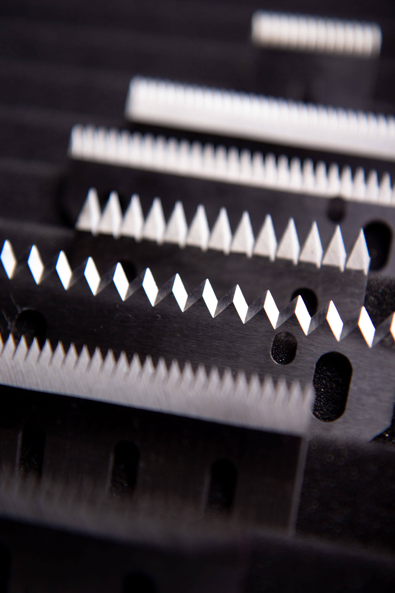 Close-up pf serrated tooth knives with sharp triangular cutting edges, manufactured by Durham Duplex for precision cutting applications.