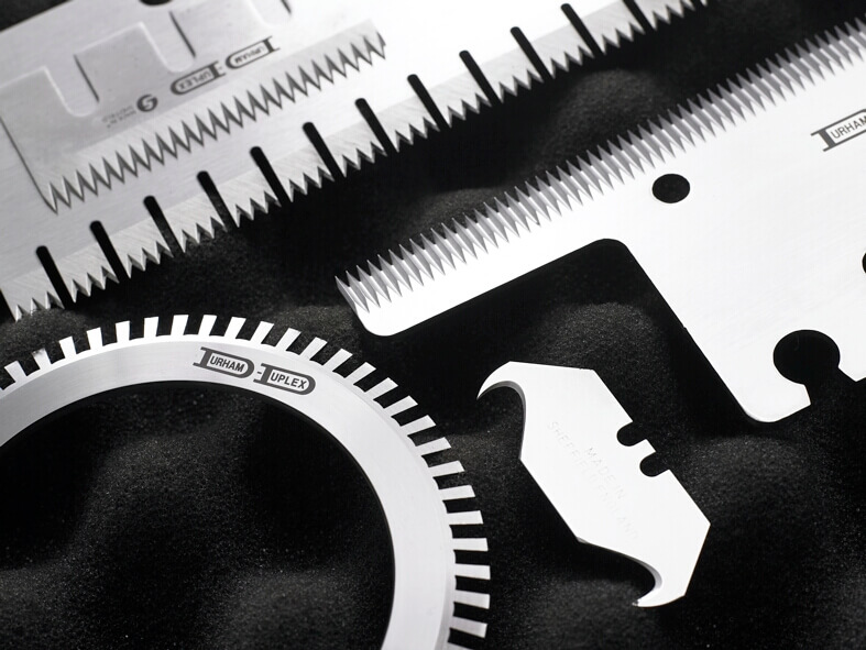 Assortment of industrial knives including serrated, hooked and circular blades, engraved with the Durham Duplex logo, used for precision cutting and packaging applications.