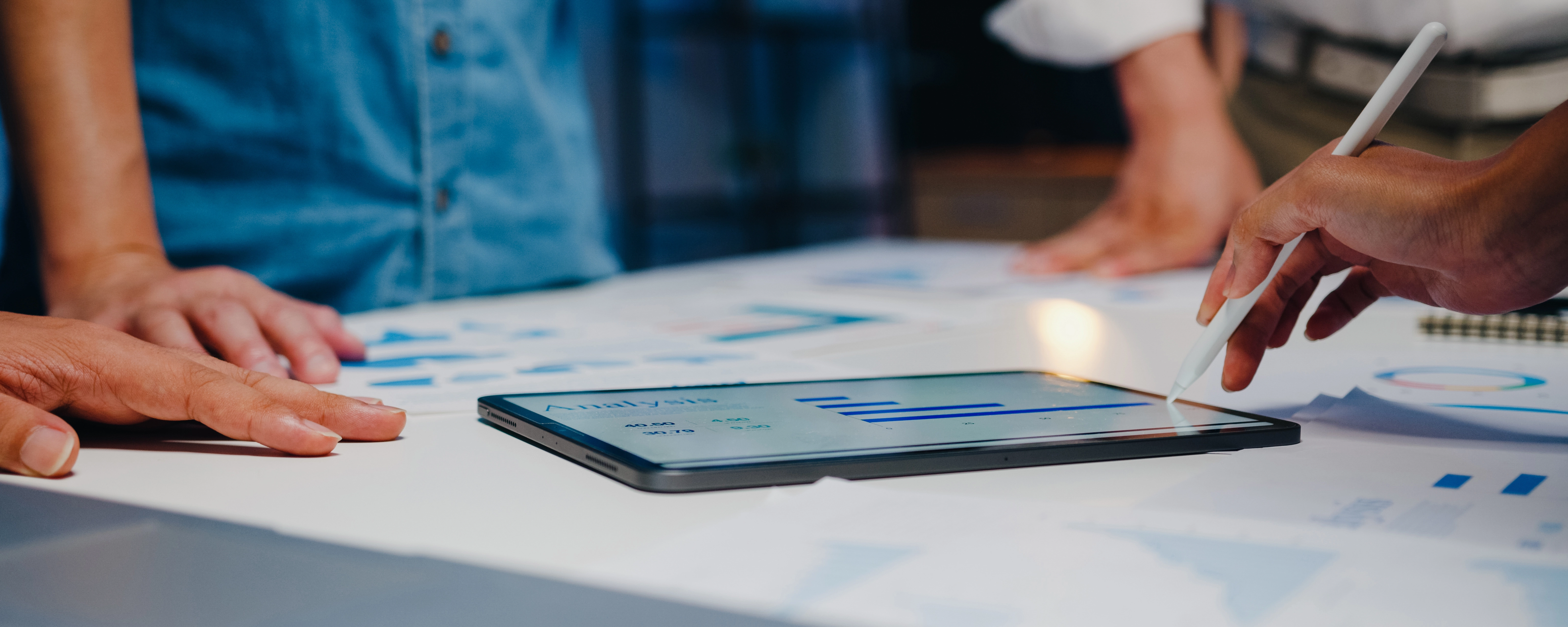 Close-up of hands using a stylus on a tablet displaying bar graphs during a business meeting.