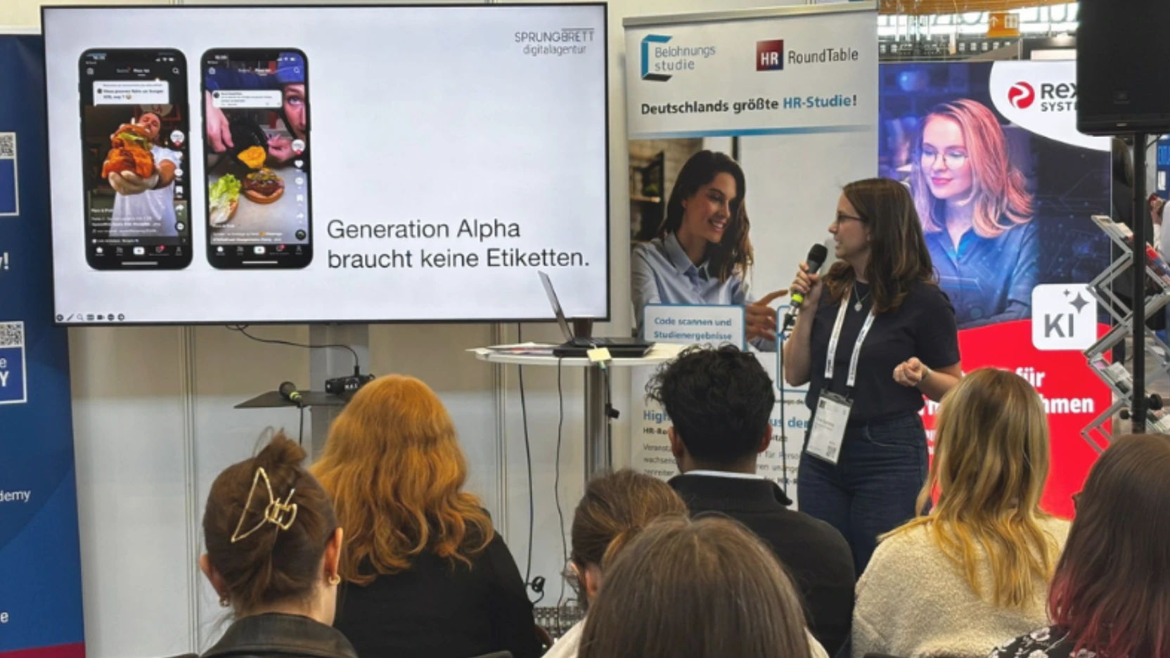Woman speaking to seated audience with a presentation slide about Generation Alpha on screen.