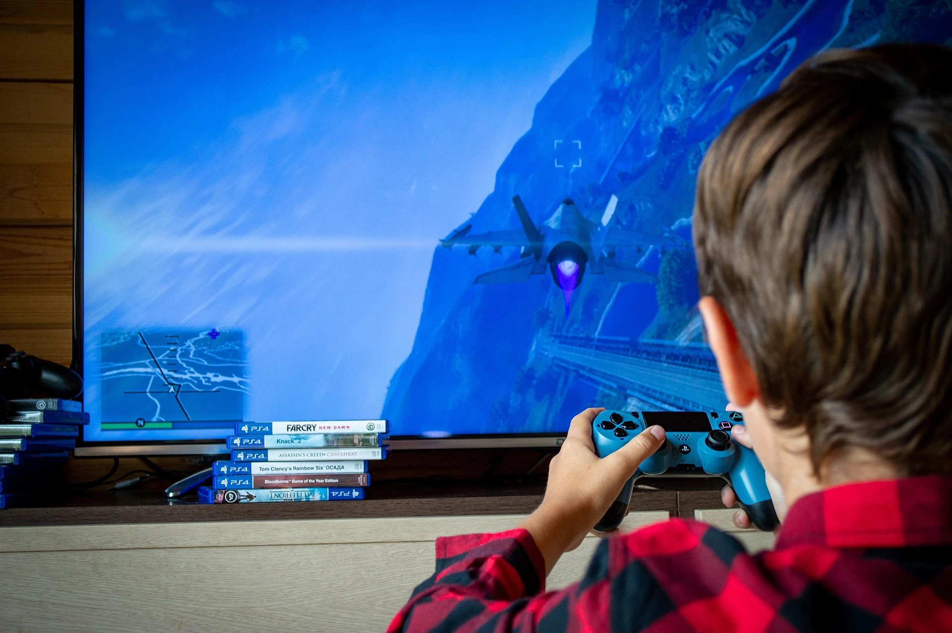 Boy holding a blue controller playing a flight video game with a jet fighter on the TV screen.