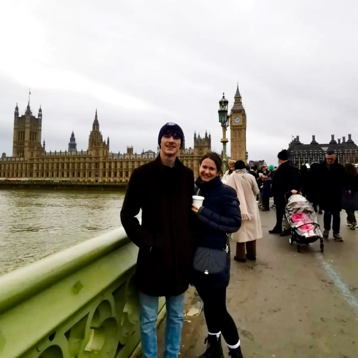 Two people smiling on a bridge in London with Big Ben and the Houses of Parliament in the background.