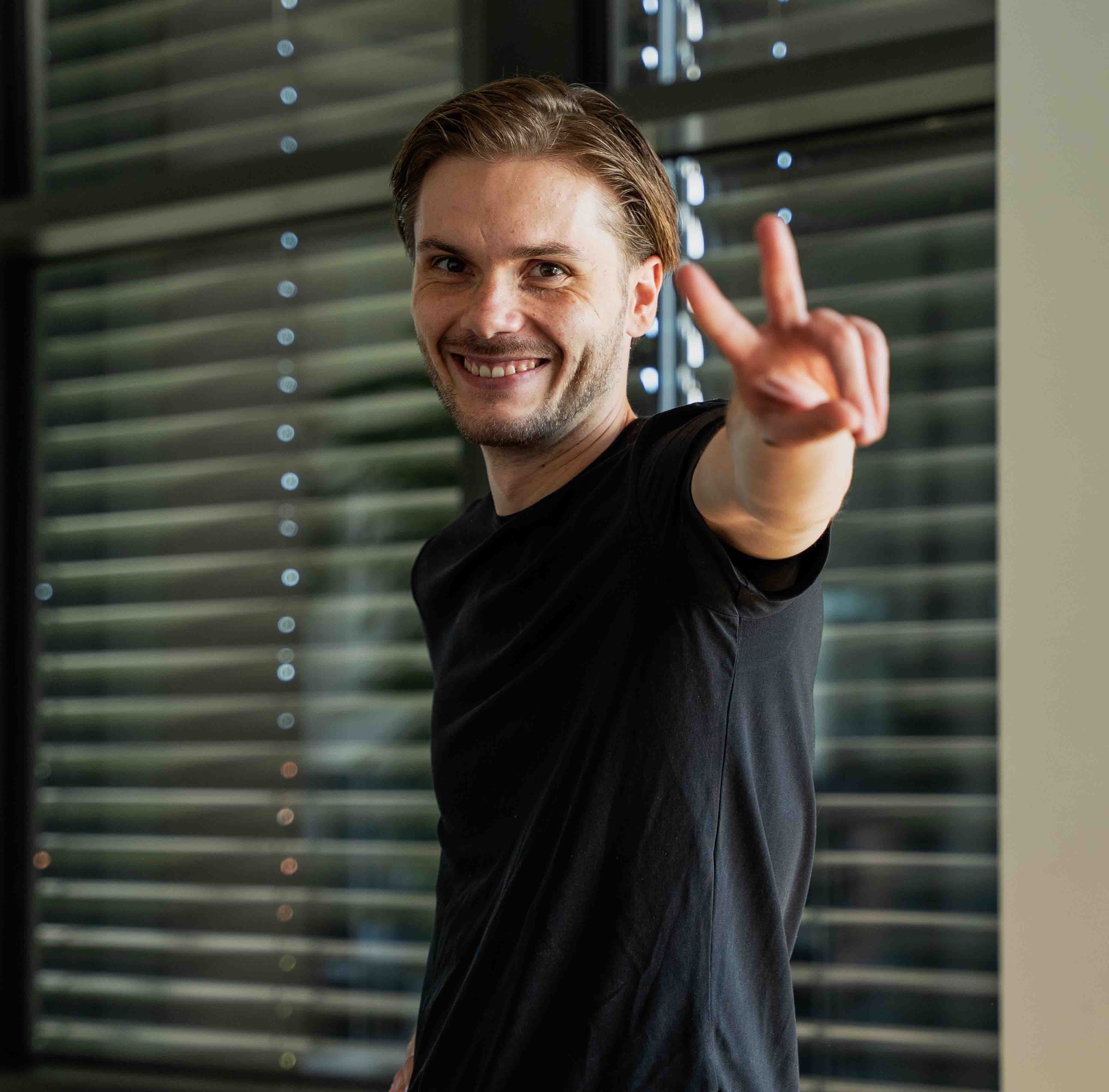 Steve Colin vom PimpUP Team zeigt lächelnd das Peace-Zeichen im Büro