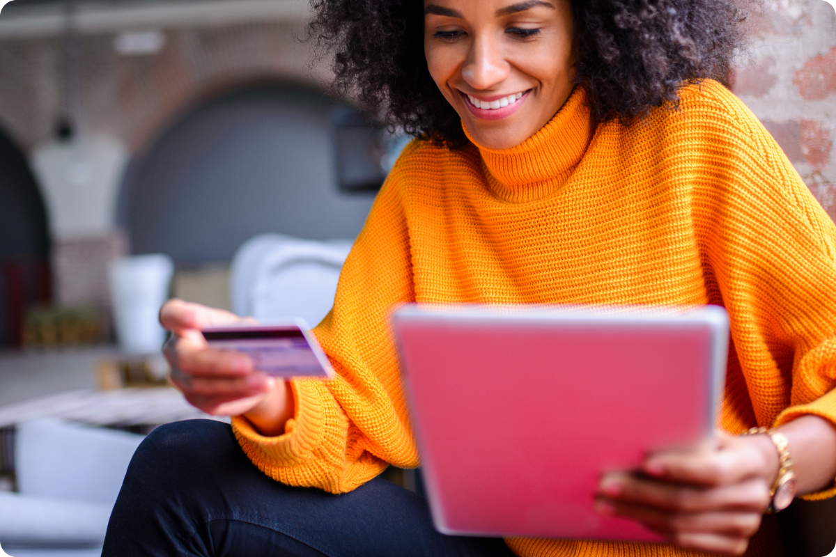 A young woman in an orange sweater is pictured holding her credit card as she makes an online donation