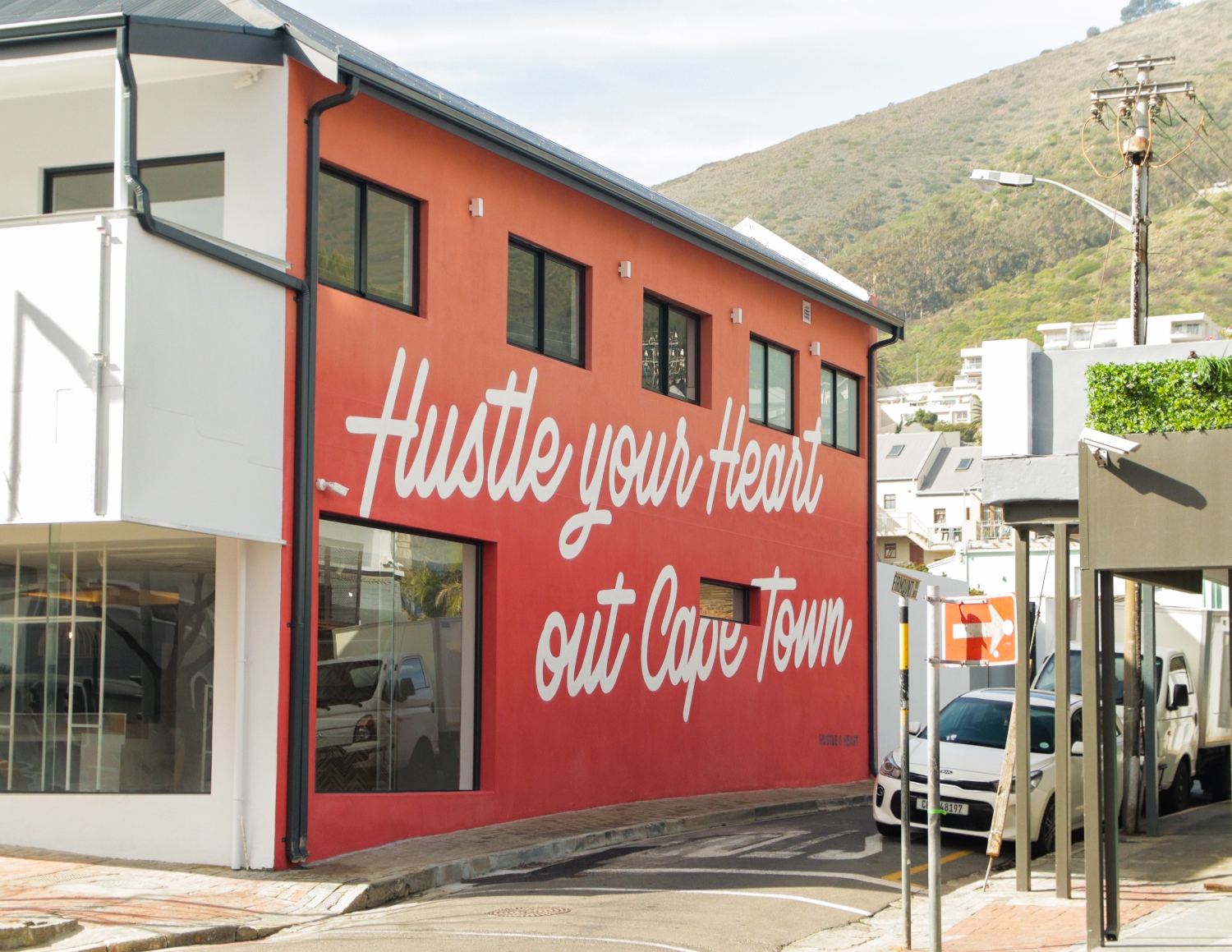 Hand-painted exterior wall sign for Hustle & Heart in Sea Point Cape Town — large white script lettering on red building by 89 Signs