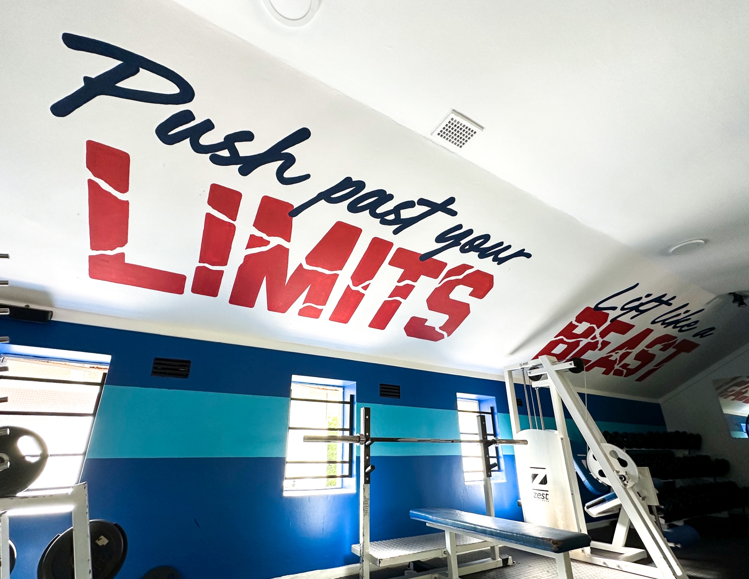 Gym interior with blue walls, weightlifting bench, and motivational text 'Push past your LIMITS' painted on the ceiling.