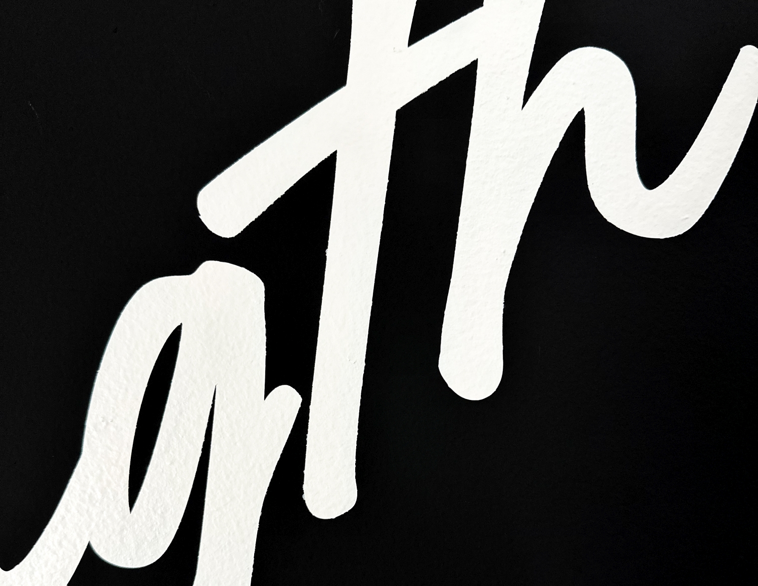 Close-up of white cursive letters painted on a black textured surface.