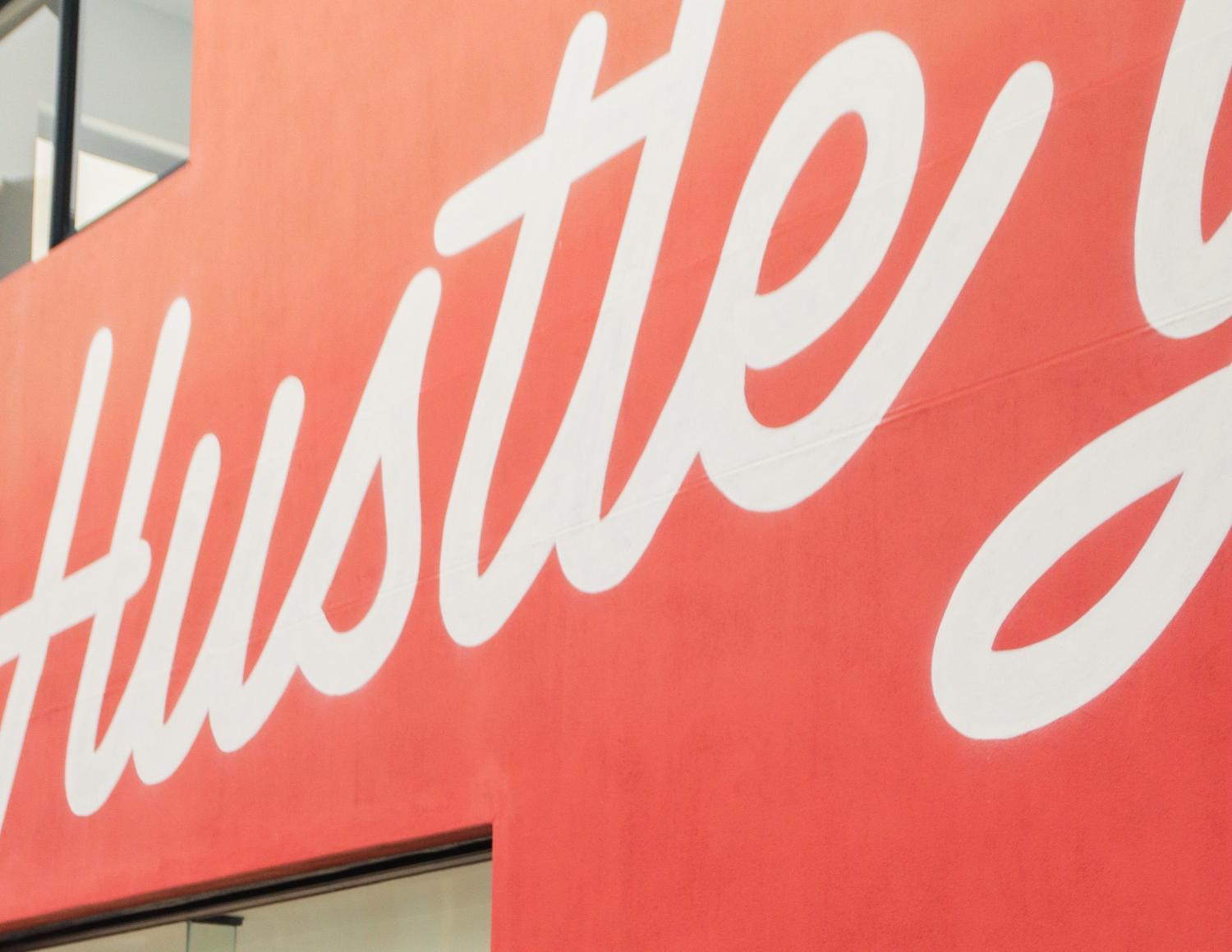 Close-up of a red wall with the large white cursive word "Hustle" painted on it.